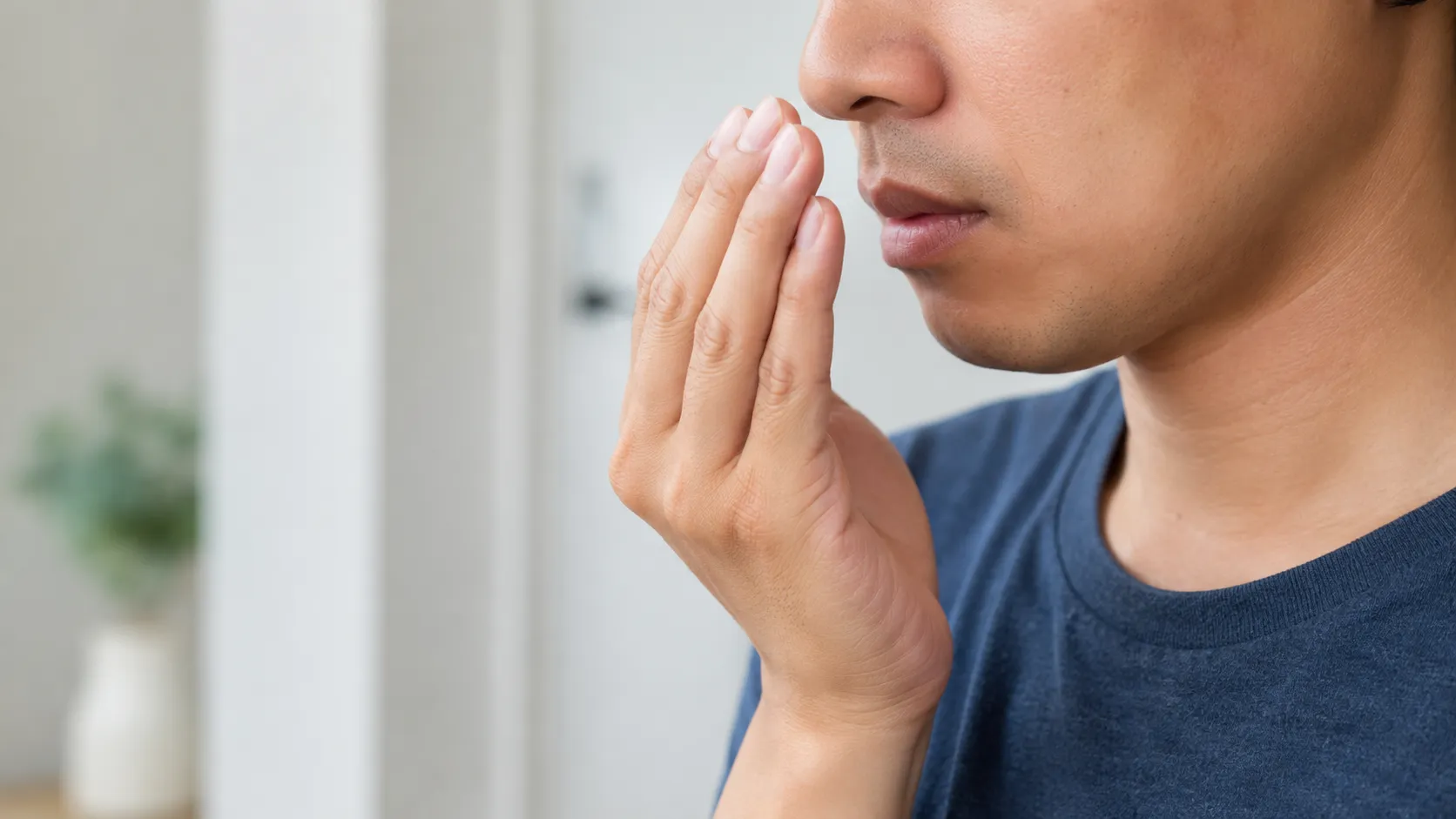 Person checking their breath with a hand close to the mouth.