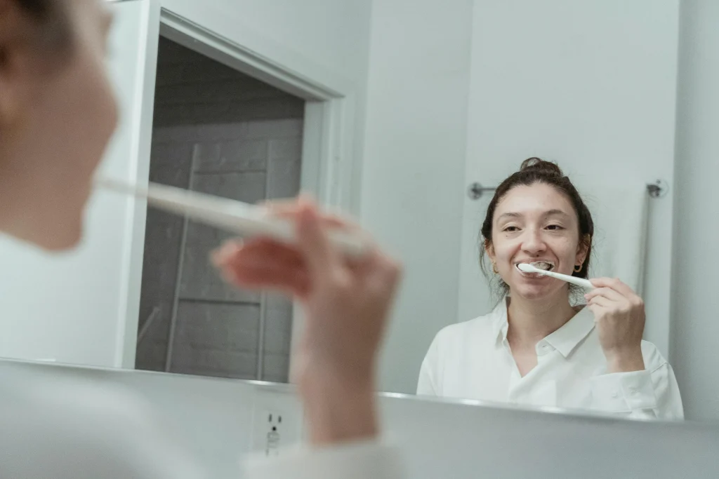 Woman brushing her teeth in the mirror during her daily oral hygiene routine.
